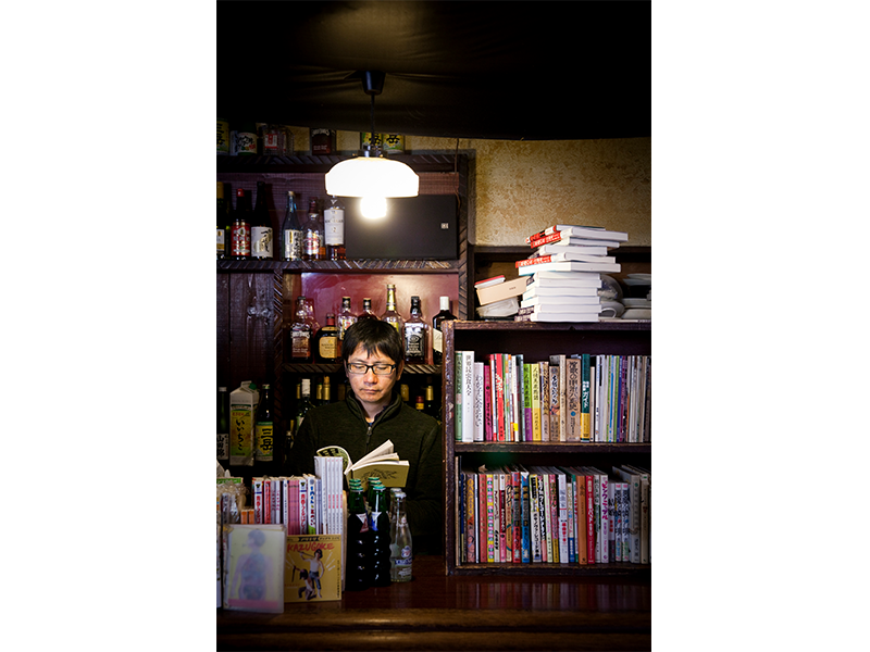 カウンターの中で本を手にする、店主の門田さん。一見、気難しそうだがそんなことはない。古本と中古バイクと相撲が好きな、1967年生まれのナイスミドルだ。