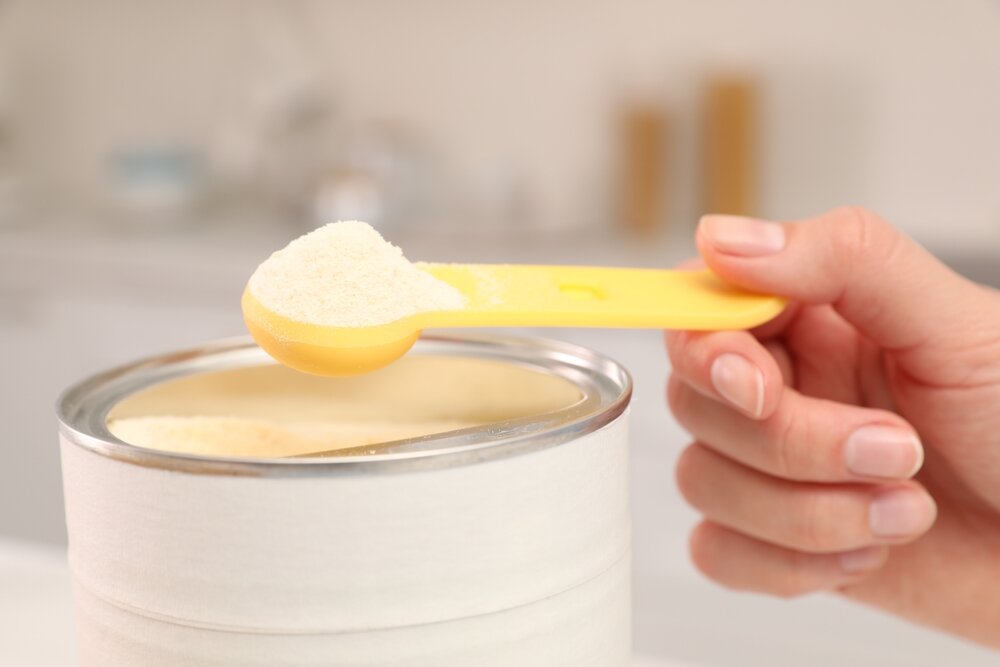 缶に入った粉ミルクをスプーンですくう人の手元