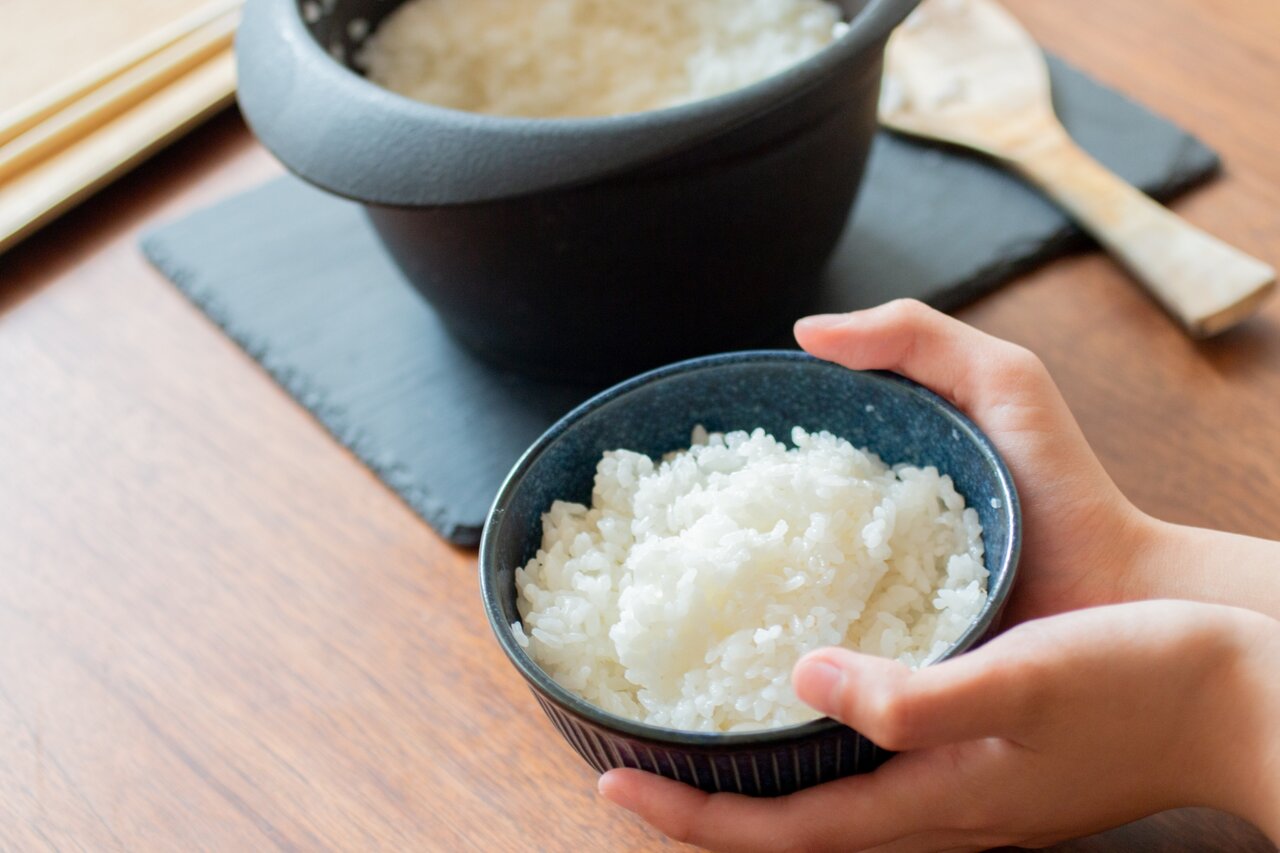 お茶碗によそった土鍋ご飯を手渡す人
