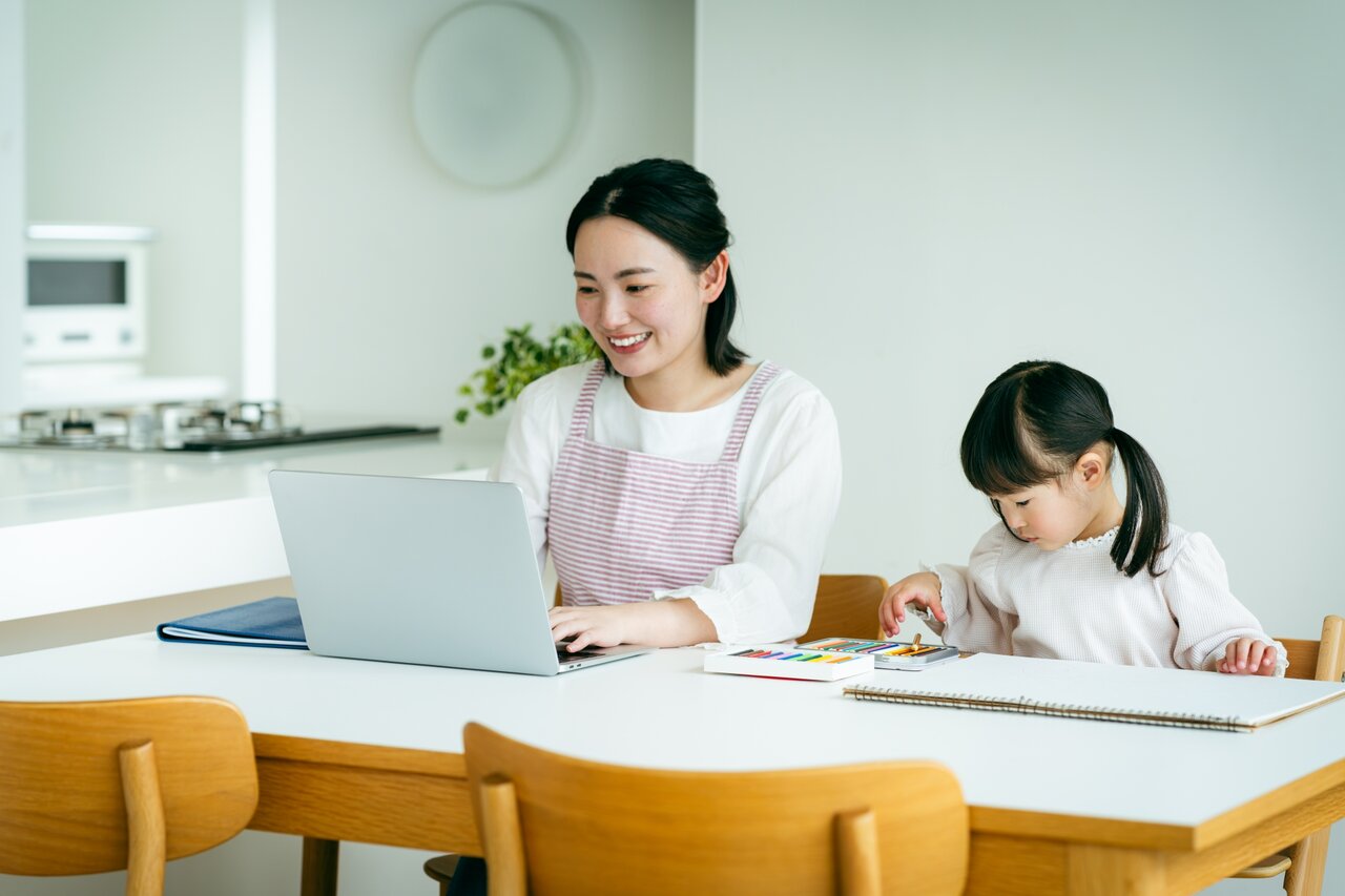 子どもの横でテレワークをするママ