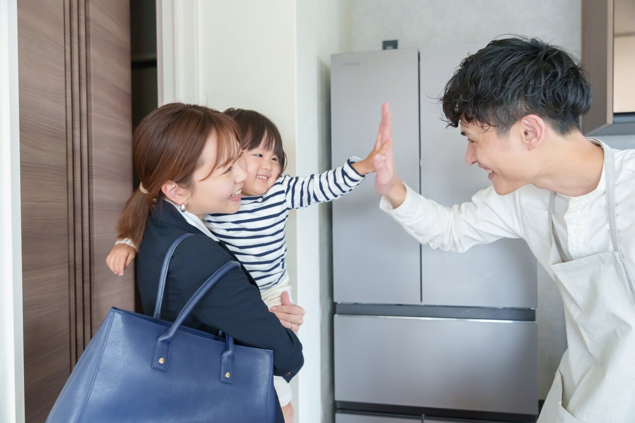 子どもを抱えて出かけるママと笑顔で見送るパパ