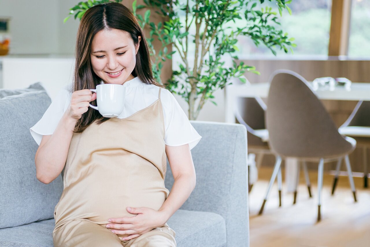 ソファに座ってドリンクを飲む妊婦
