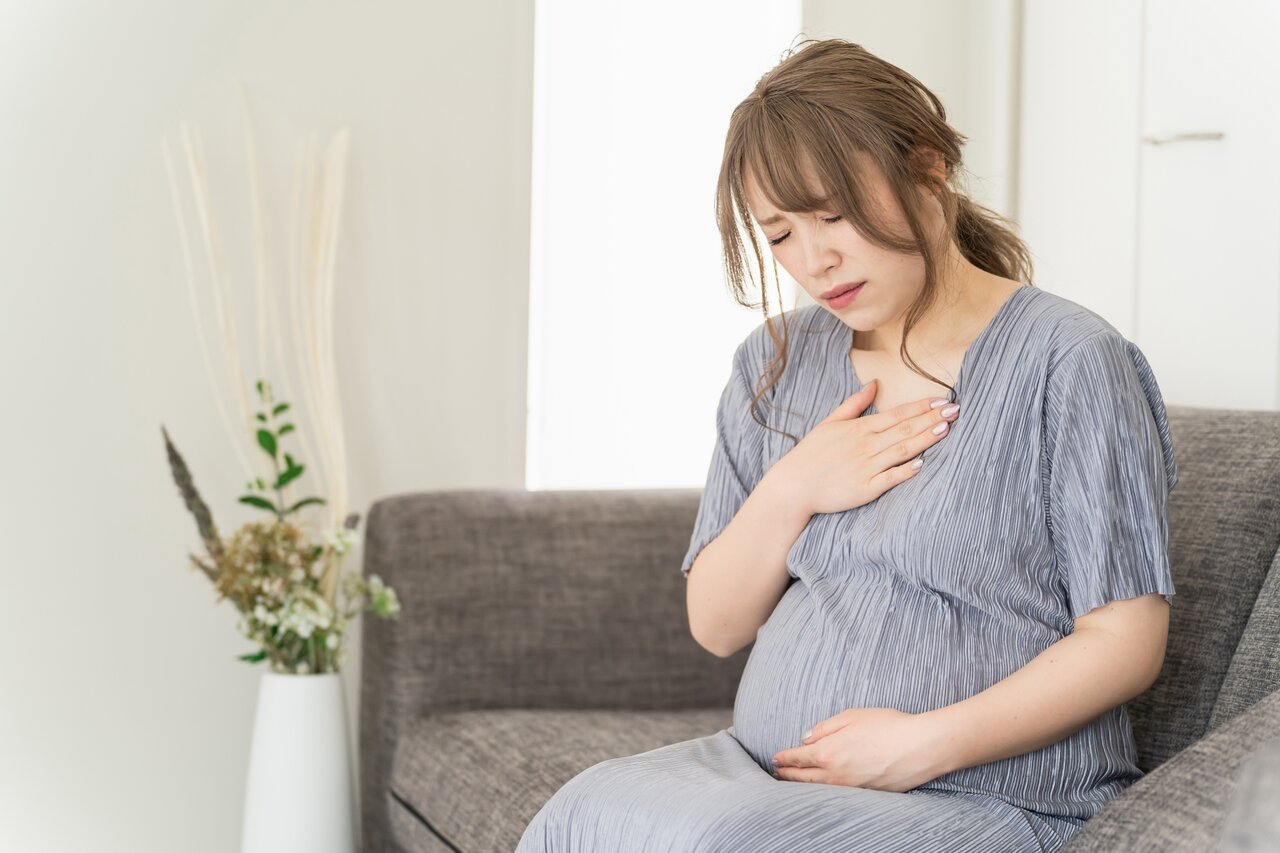 ソファに座ってつらそうな表情を浮かべる妊婦