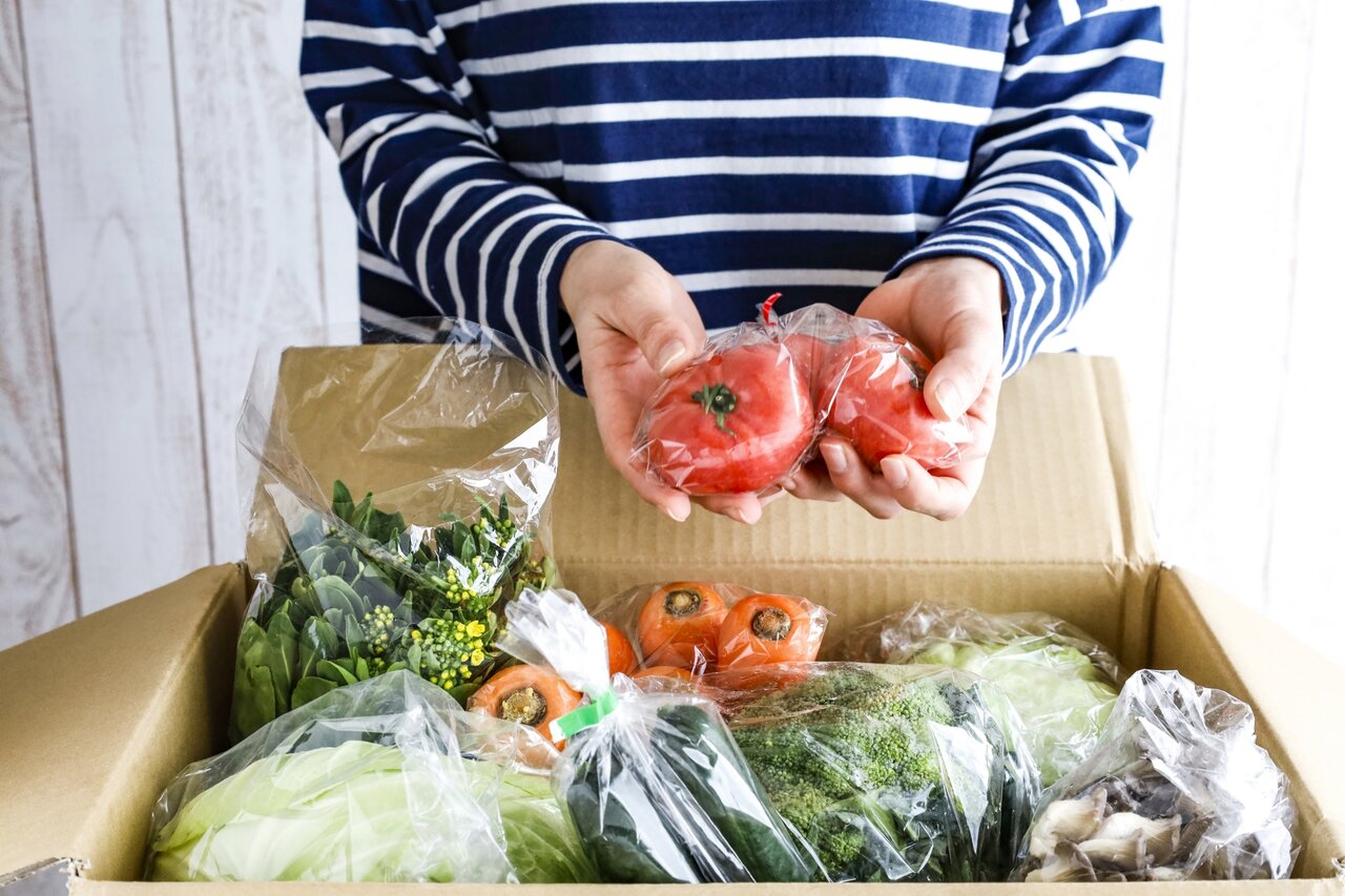 野菜がたくさん入った段ボールからトマトを取り出す女性