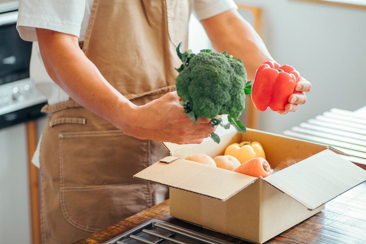 キッチンでダンボールから野菜を取り出す男性