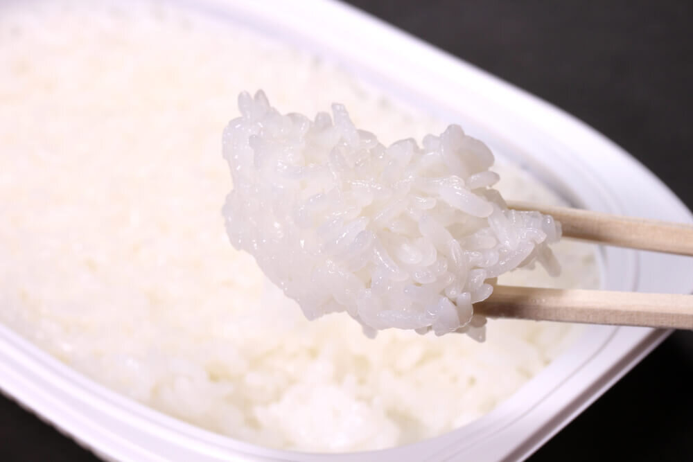 箸で持ち上げられたパックご飯