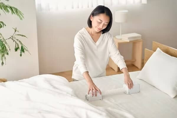 布団乾燥機をベッドの上に設置する女性