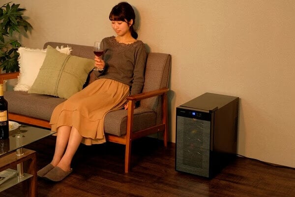 ワインセラーが置かれた部屋でワインを飲む女性