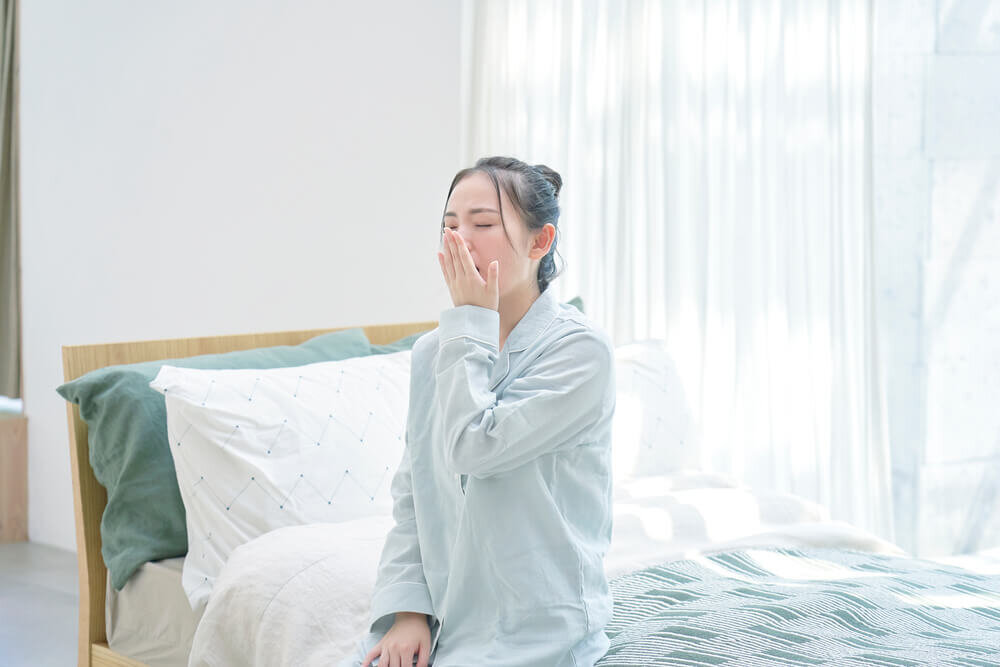 ベッドに座りあくびをする女性