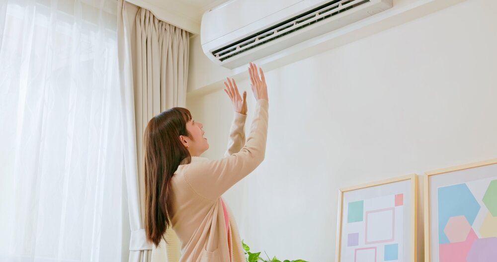 エヤコンの風を手のひらで感じる女性