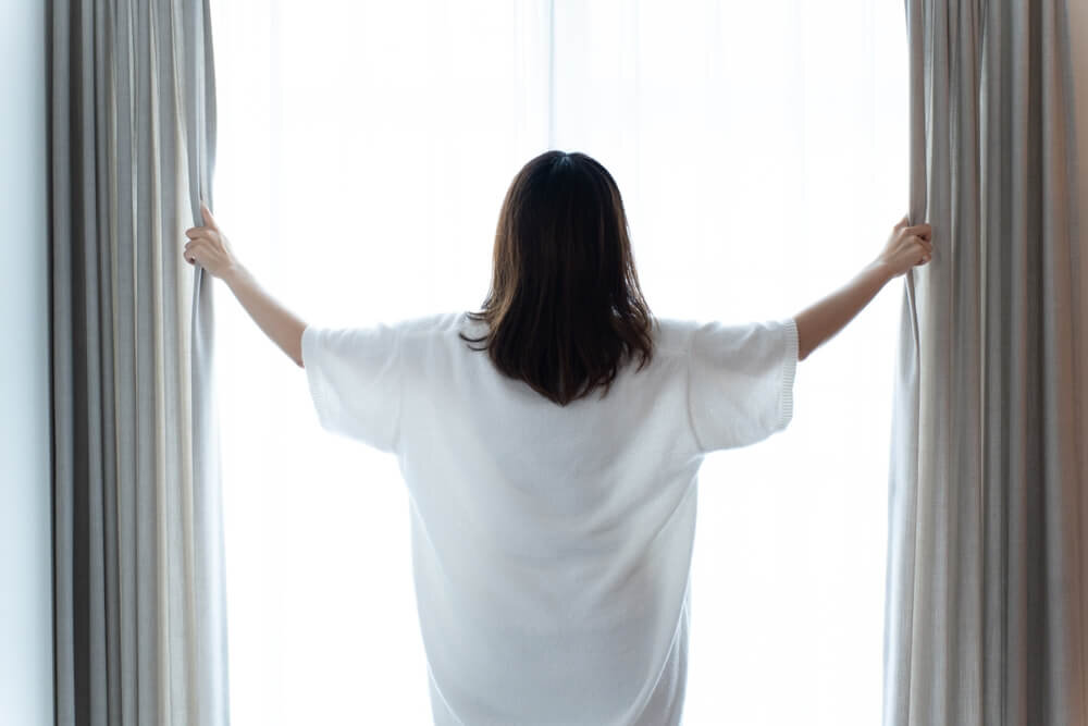 カーテンを開ける白いシャツを着た女性