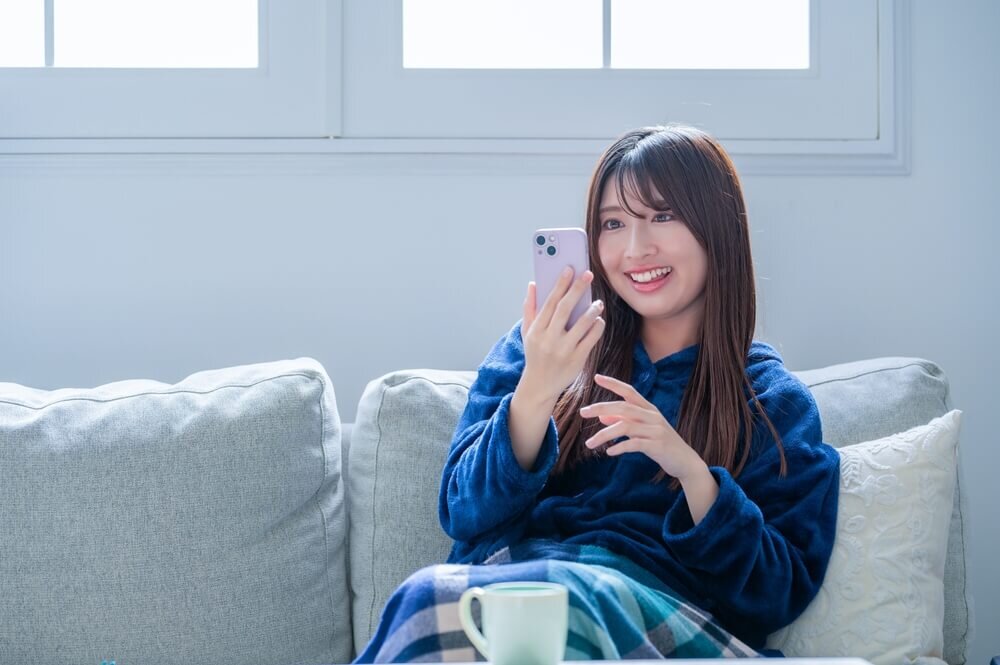 ソファに座りスマホを見る女性