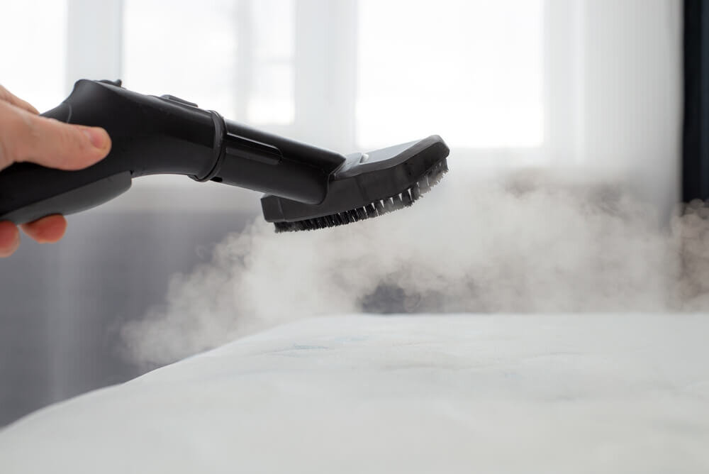 マットレスをスチームで掃除する人の手