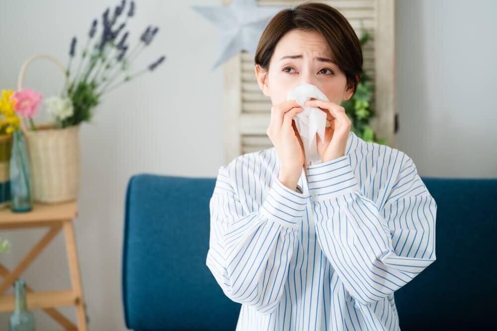 花に囲まれた部屋で鼻をかむ女性