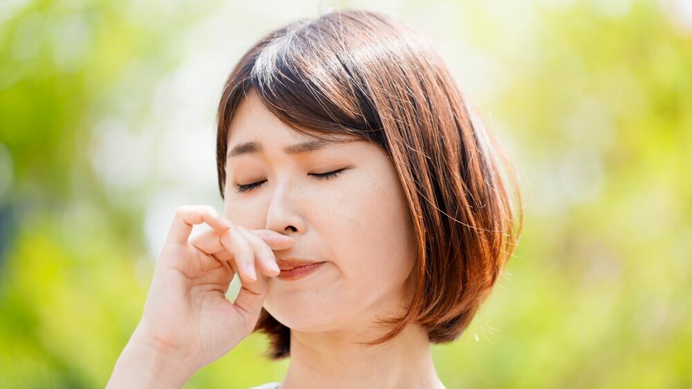 木に囲まれた屋外で鼻を触る女性