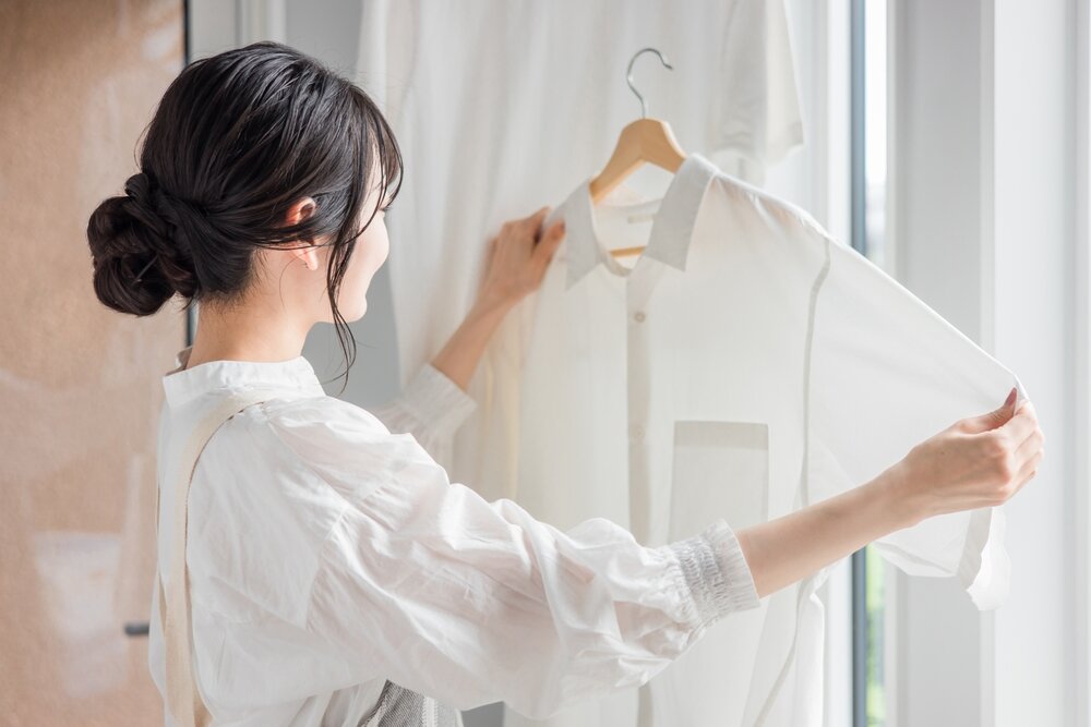ハンガーにかかった白いシャツを持つ女性
