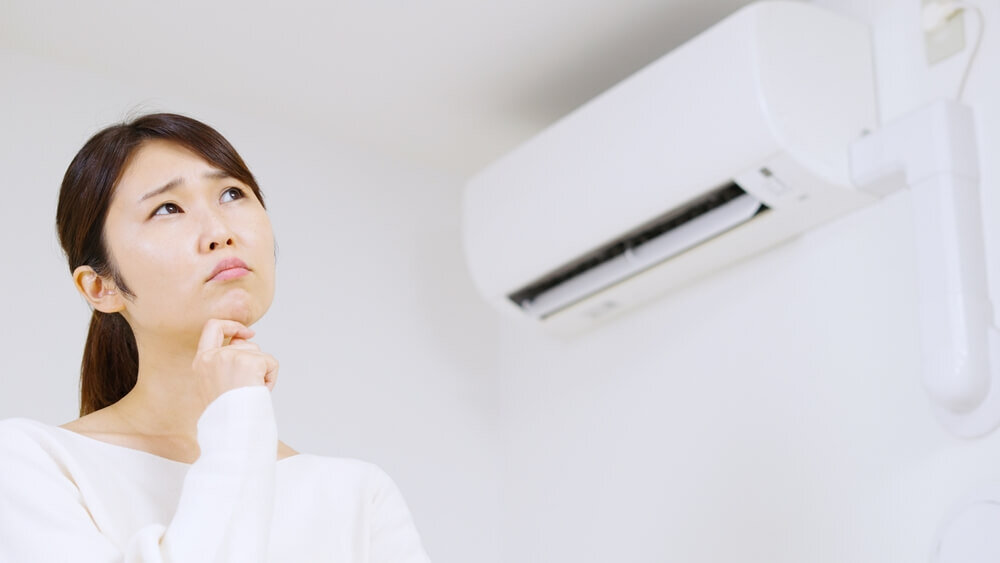 エアコンの前で首を傾げる女性