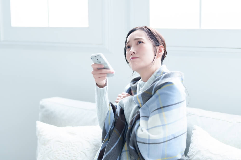 凍えながらエアコンのリモコンを操作する女性