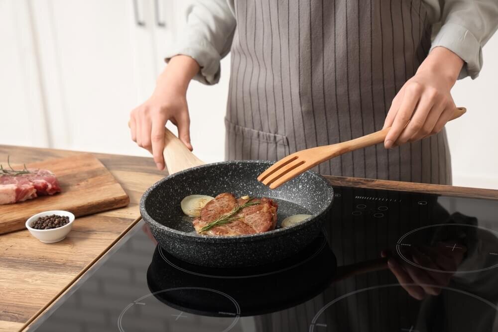 木のフォークを持ってフライパンでステーキを焼く人