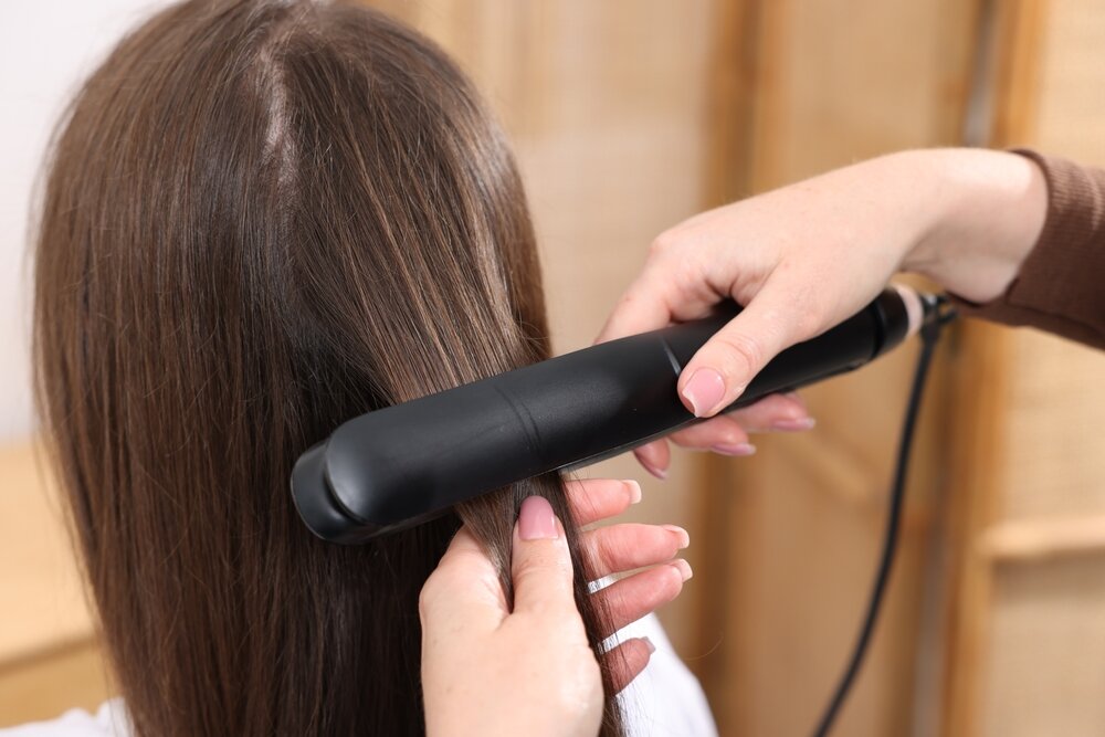 ヘアアイロンで髪をストレートにする女性
