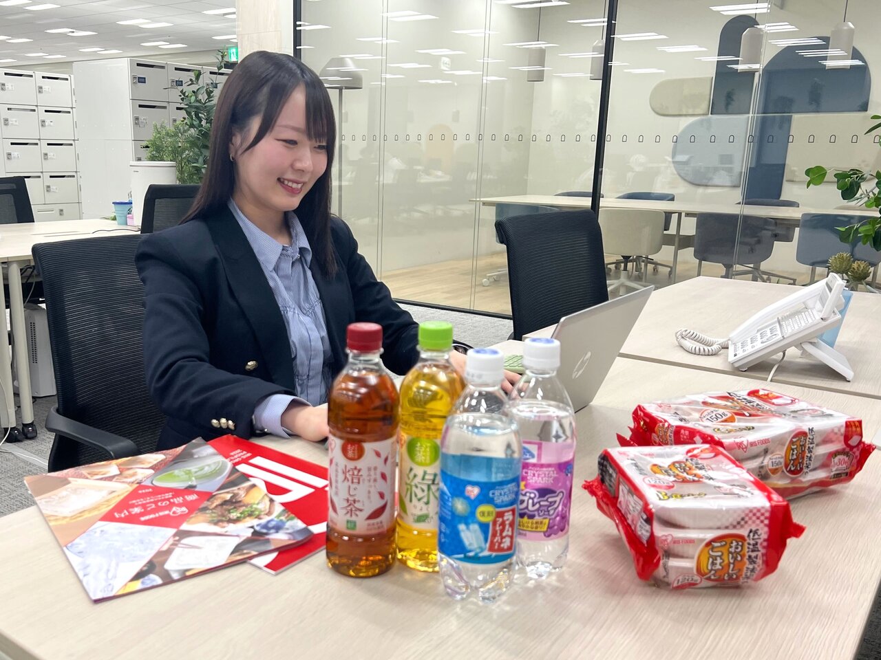 デスクワーク中の近藤さんとアイリスフーズの商品