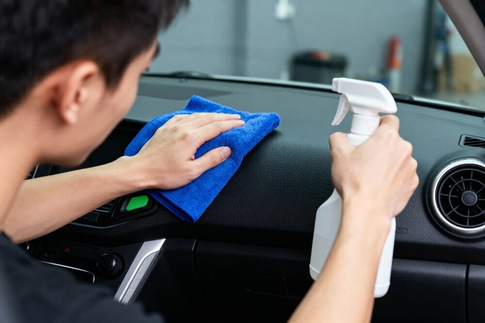 スプレーとクロスで車を掃除する男性