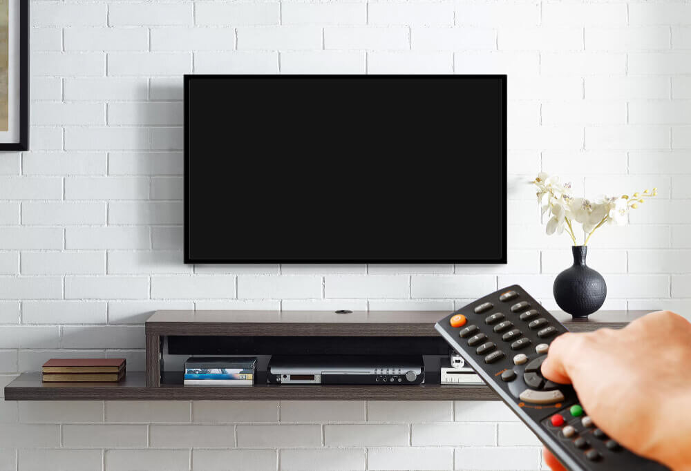 リモコンを持った手元と壁掛けテレビ