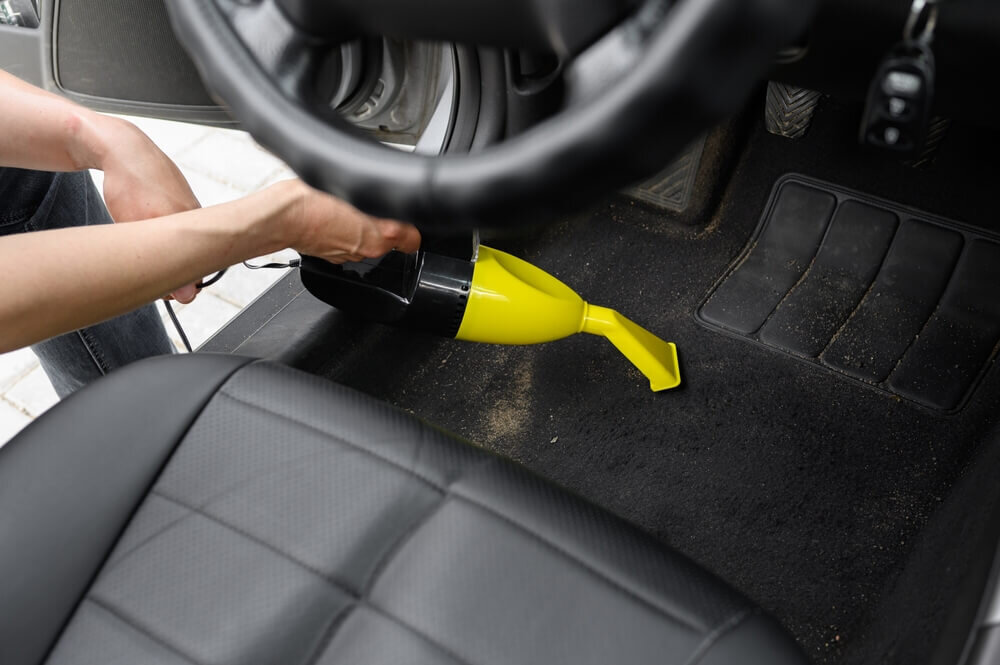 車のフロアに掃除機をかける人の手元