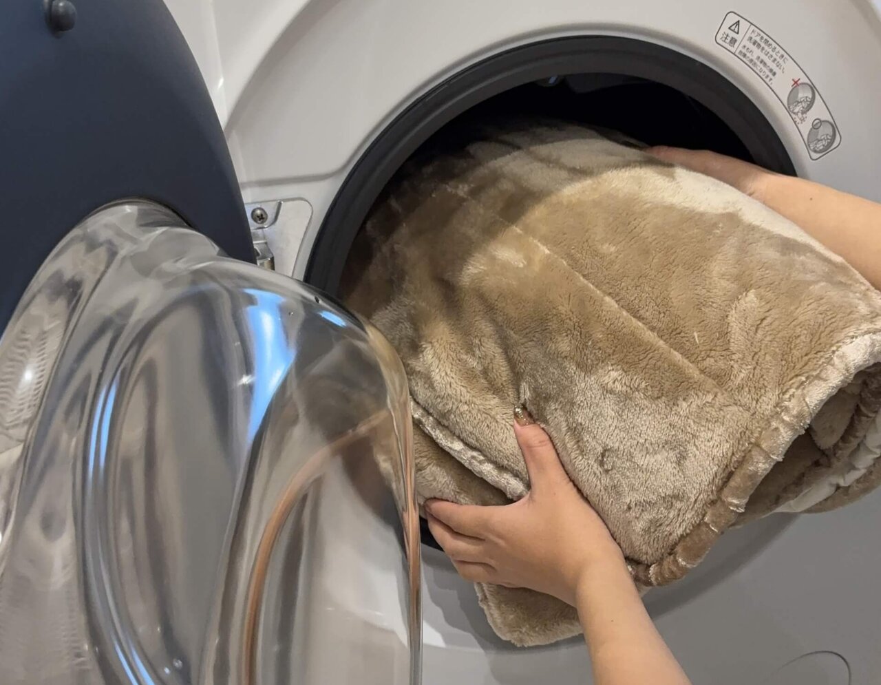 丸めた毛布をドラム式洗濯機に入れる人