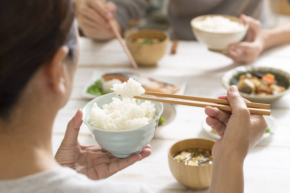 料理が並んだ食卓で白米を食べる女性