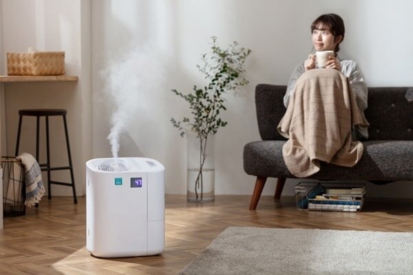 加湿器が置かれたリビングのソファで暖をとる女性