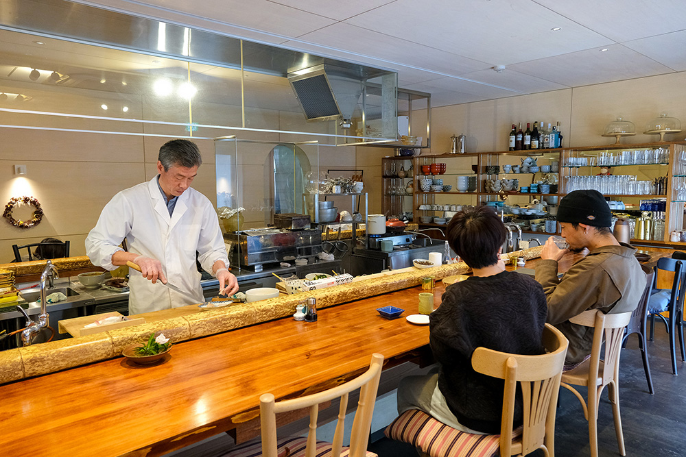 カウンター席のお客様の前で、オープンキッチンで調理する店主の姿