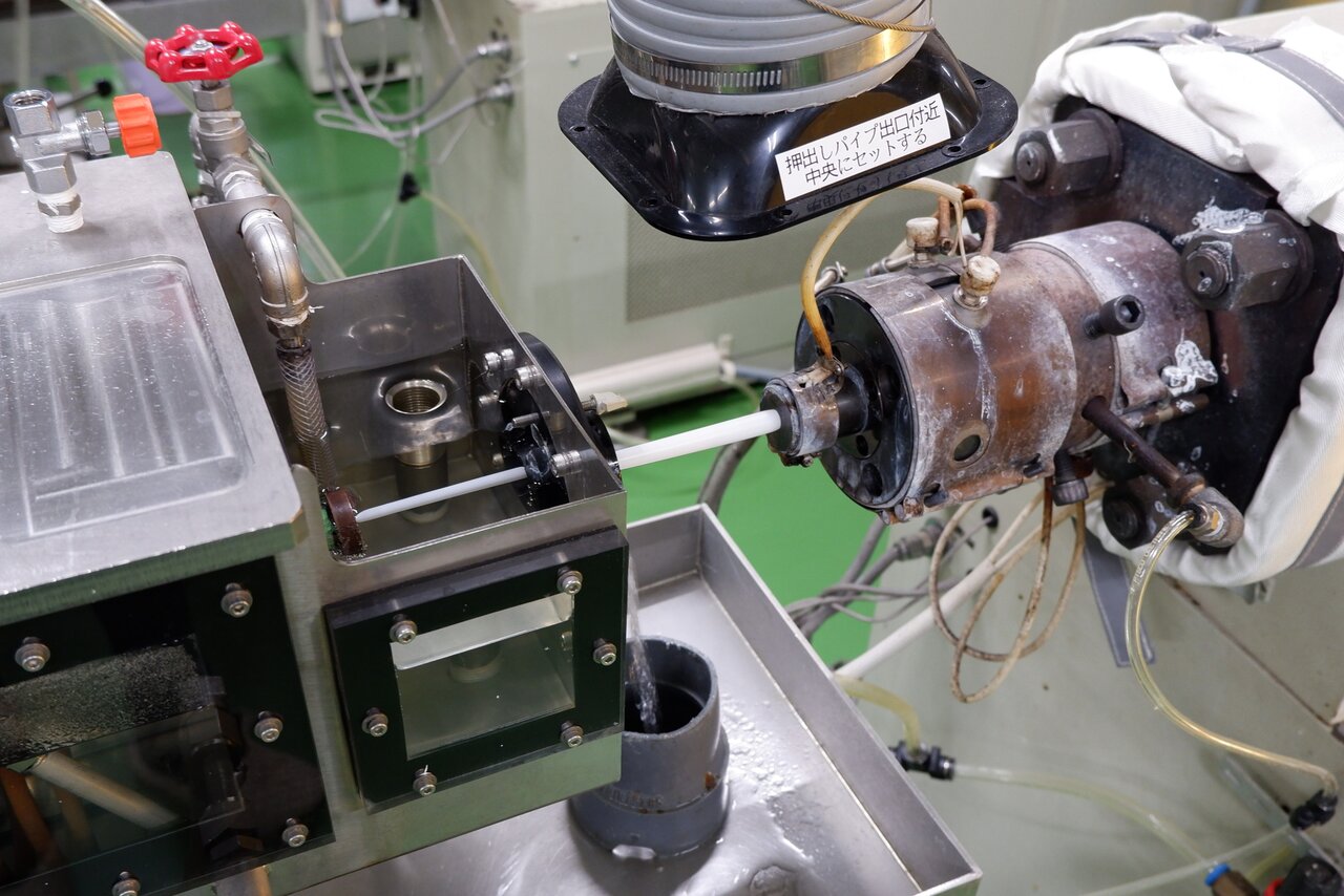 ストローを成形する様子（上）と口金から押し出されるストロー（下）。押出直後に水で冷却されて凝固する