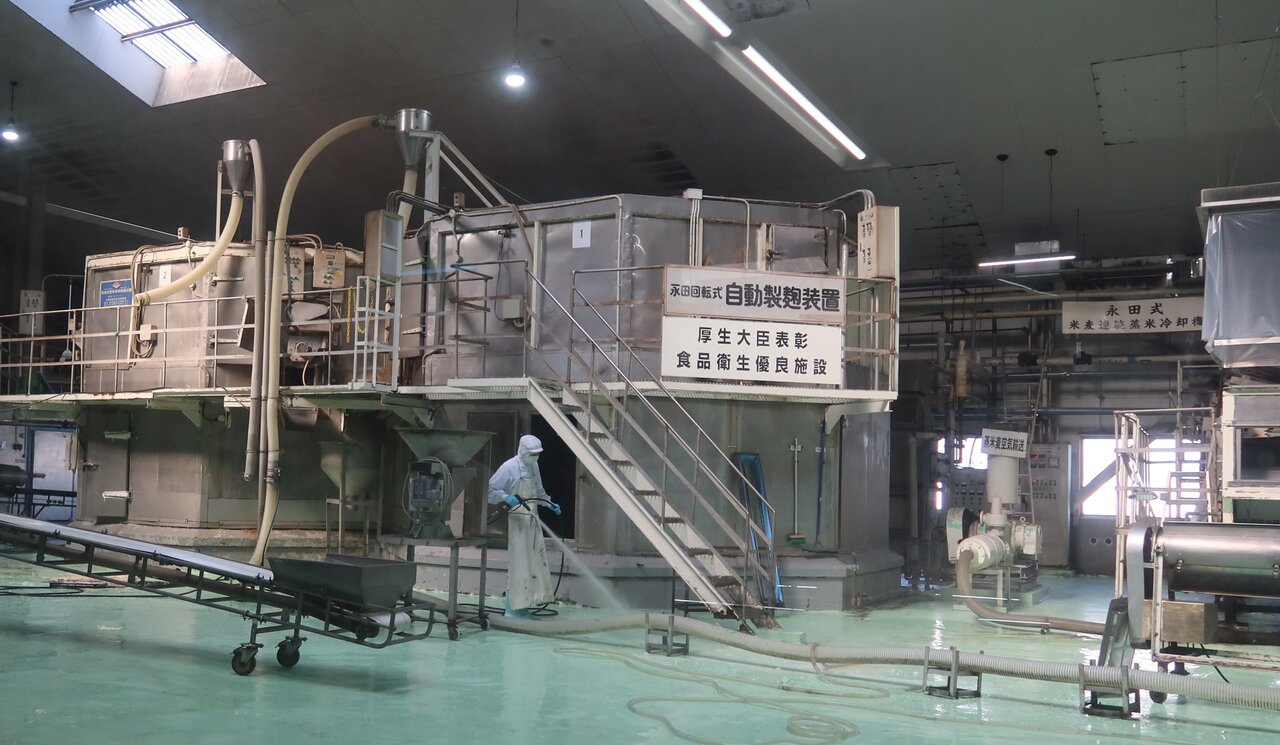 「円盤回転製麹装置」と念入りに機械洗浄・清掃を行う作業員 （写真提供：サクラみそ食品）