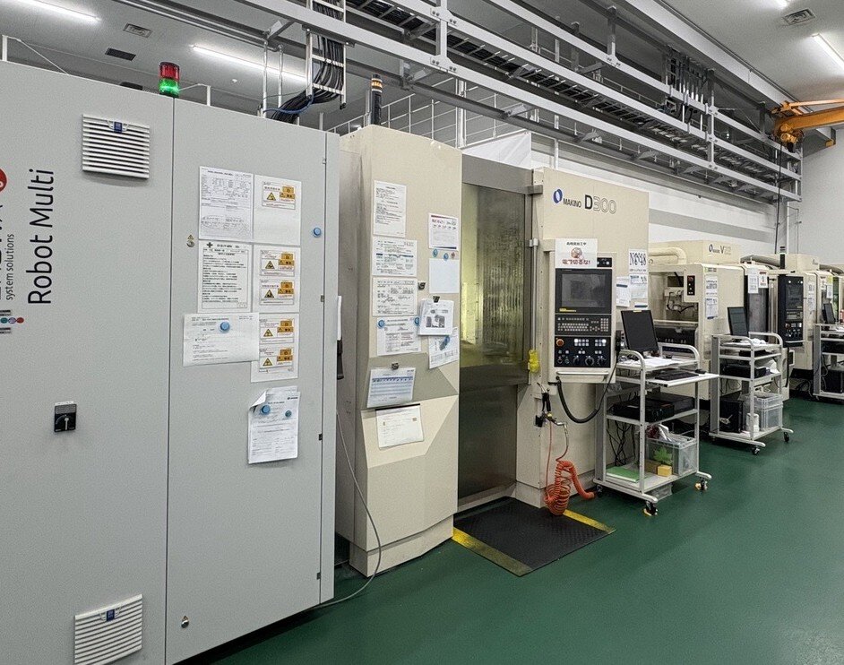 5軸制御立形マシニングセンタD300と立形マシニングセンタV22（牧野 フライス製作所）。自動化設備と連動している。