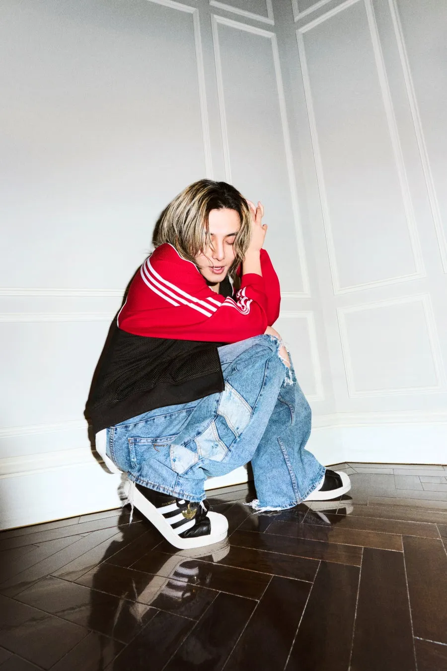 赤と白のジャケットと青いジーンズを着た人が、床にしゃがんでいる写真です。