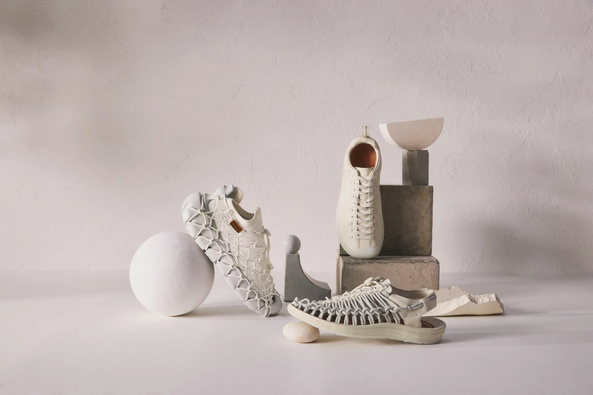 白いスニーカーとサンダルが、白い球体、幾何学的なオブジェと共に配置された写真。