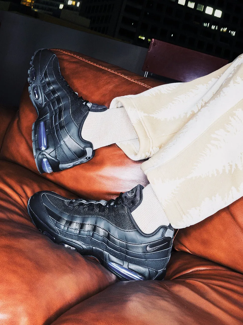 黒いスニーカーを履いた人の足元の写真。革張りのソファに座っており、夜景が見える。