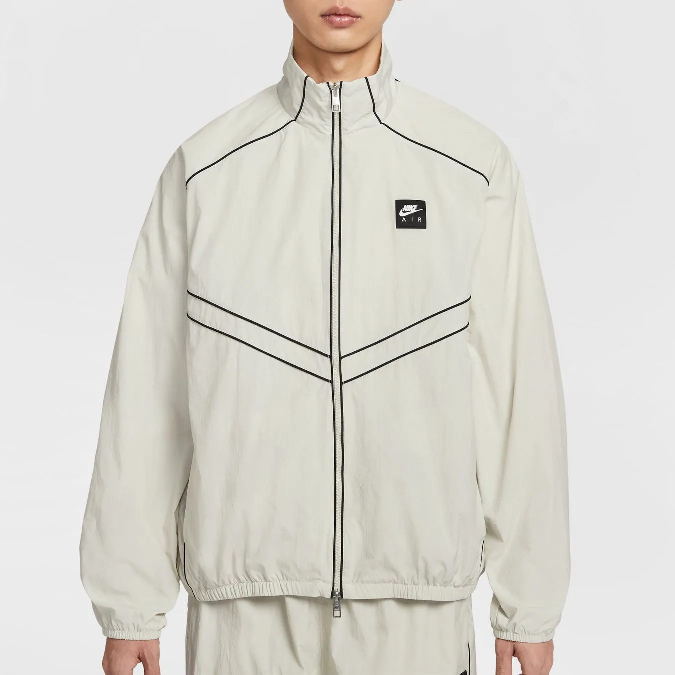 白を基調としたナイキのジャケットを着た男性の正面写真です。ジャケットには黒のラインのアクセントと、胸にナイキのロゴパッチが付いています。