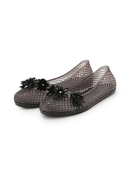 2つのグレーのフラットシューズのクローズアップ写真。各靴の前面には、装飾的な黒い花の装飾が付いています。