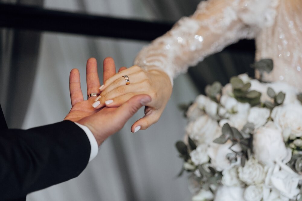 右手の薬指に結婚指輪を着けるカップル