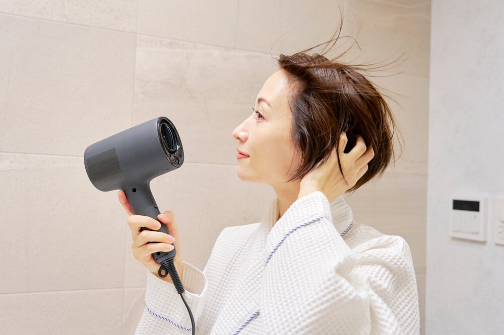自分の髪をドライヤーで乾かしている女性の写真