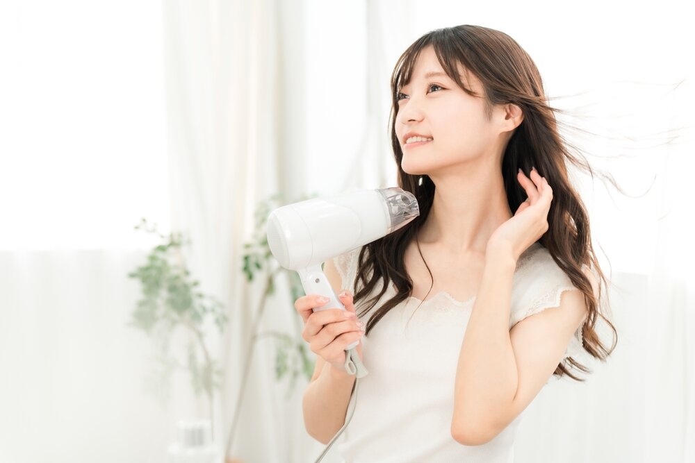 日本人の女性がパーマがかかった髪の毛をドライヤーで乾かしている写真