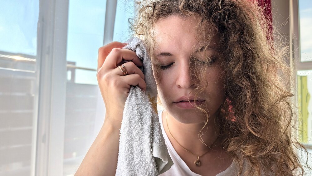 パーマがかかった髪の毛の女性がタオルで顔と髪の毛を拭いている写真