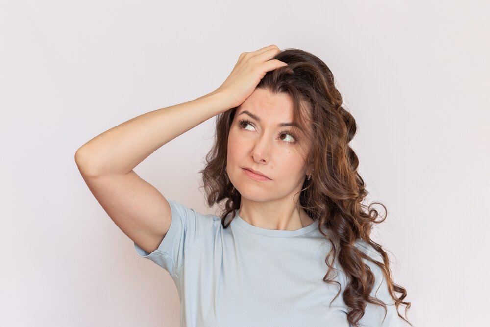 髪にパーマがかかった女性が右斜め上を見つめて考え事をしているような写真