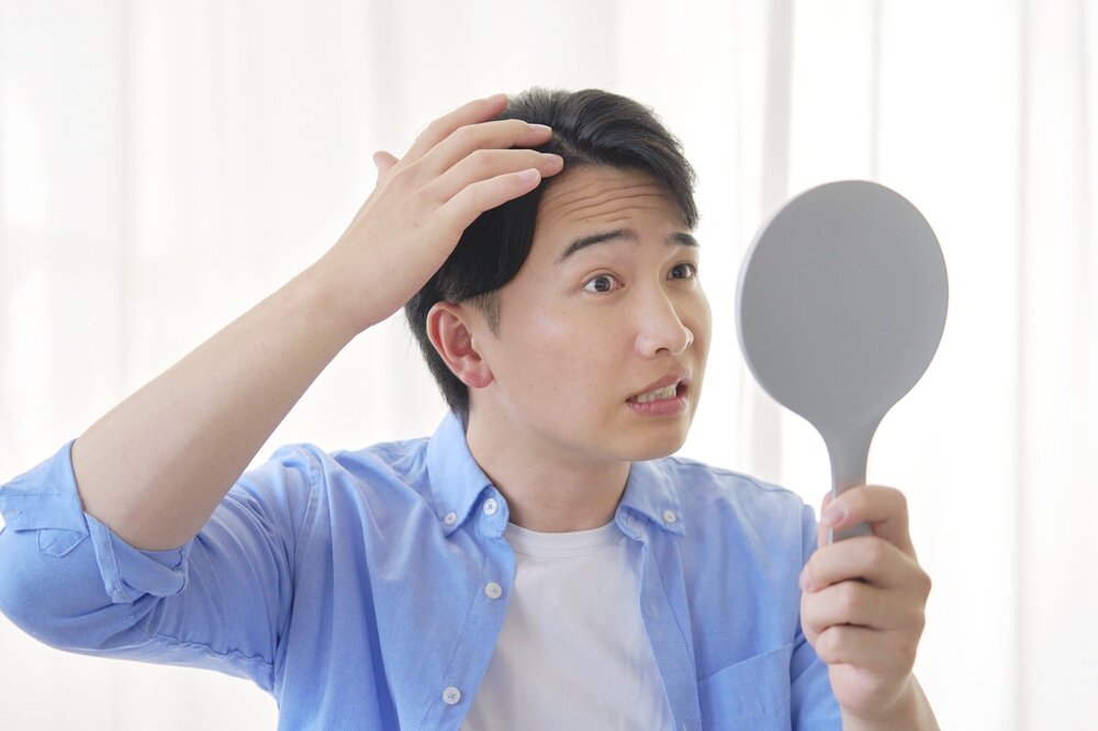 自分の髪の毛を手鏡で見ている人の写真
