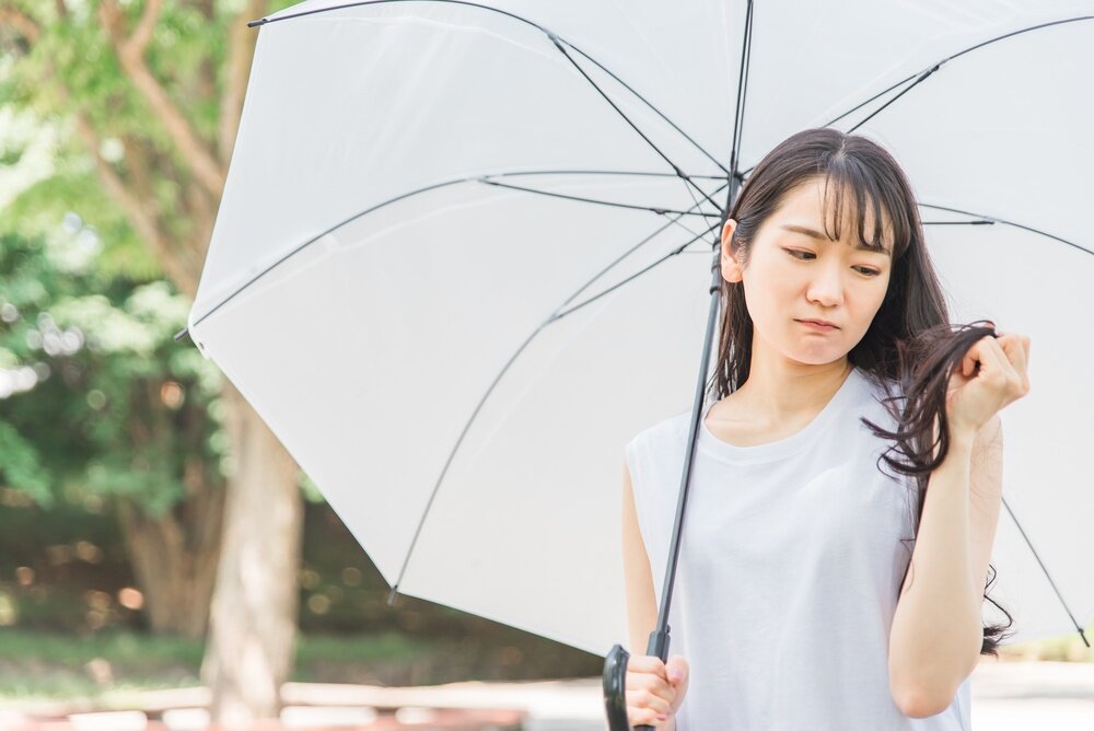 傘を差している女性が自分の毛先を持って悩んでいるような写真