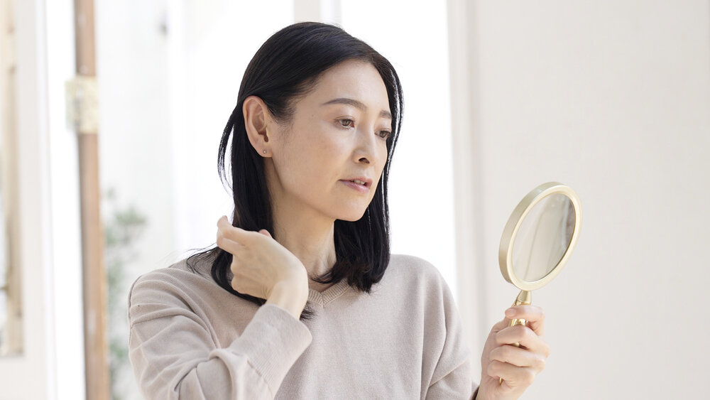 手鏡を持って髪の毛を見ている中年女性の写真