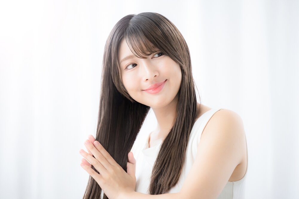 アジア人女性が自分の髪の毛を両手で挟んでケアしている写真