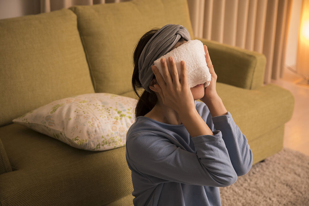 蒸しタオルで目の周りを温める女性